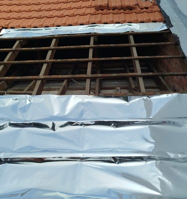 A roof repair project showing exposed wooden battens and reflective foil insulation under terracotta tiles.