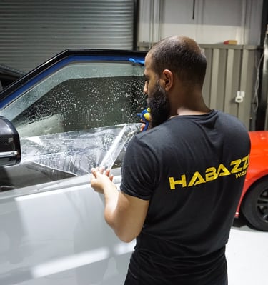 Professional auto technician applying tints film to a white SUV window for UV protection.