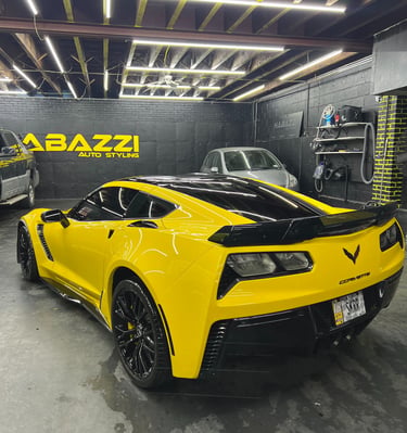 Yellow Chevrolet Corvette C7 with black trim inside a professional auto styling and car detailing garage.