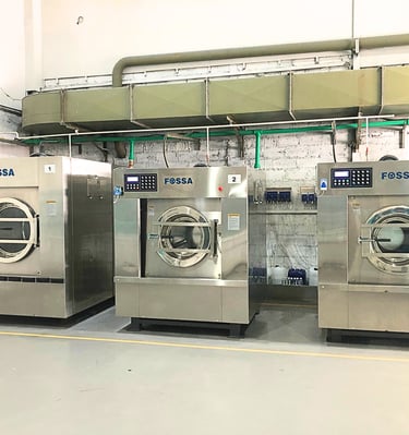 Three large stainless steel industrial Fossa washing machines in a commercial laundry facility.