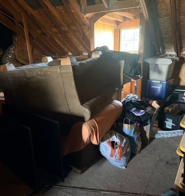 An attic full of junk including a couch and chair and a bunch of trash bags