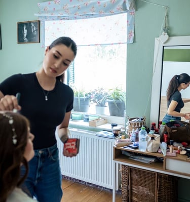 Bride sitting at vanity while makeup artist adds finishing touches — elegant bridal photo prep