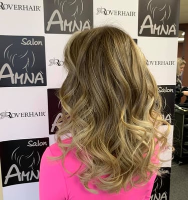 Woman with long blonde wavy hair highlighting professional hair color services at Salon Amna.