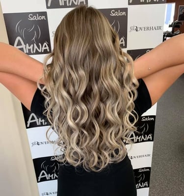 Woman with long blonde balayage hair styled in loose curls at Salon Amna.