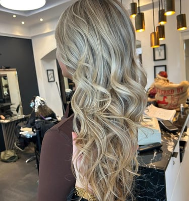 Woman with long blonde balayage hair featuring loose waves and highlights styled in a professional hair salon.