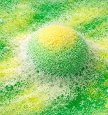 Oversized bath bomb releasing green and yellow foam with soft, creamy fizz.