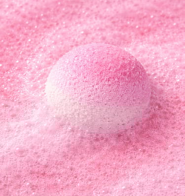 Large pink bath bomb surrounded by fluffy foam and gentle fizz.