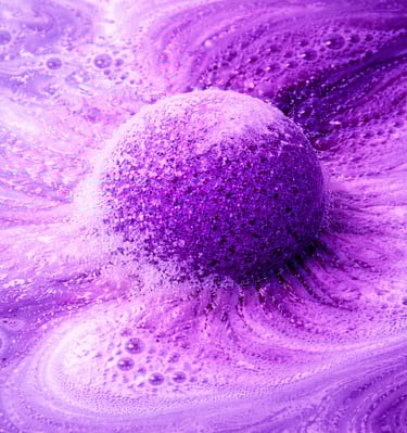 Extra large purple bath bomb fizzing in water with thick foam and cloud-like bubbles.