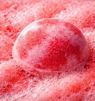 Oversized red and pink bath bomb creating bold foam and intense fizz in water.