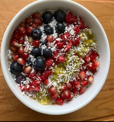 A healthy breakfast bowl topped with blueberries, pomegranate seeds, shredded coconut, and kiwi fruit.