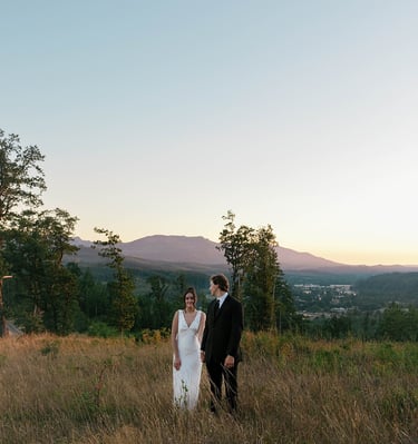 A bride and groom standing in a grassy field during a mountain sunset wedding.