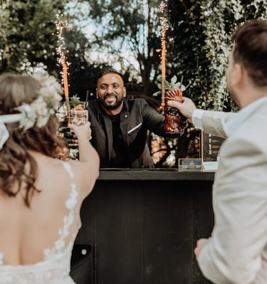 Professional mobile bartender serving tiki cocktails with sparklers to a bride and groom at an outdoor wedding.