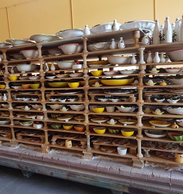 Handmade ceramic pottery and painted bowls drying on wooden racks in an Italian artisan workshop.