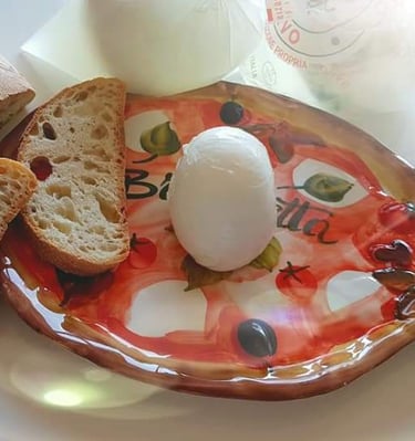 Fresh mozzarella cheese ball on a decorative ceramic board with slices of crusty Italian bread.