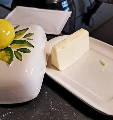 A stick of fresh butter on a white ceramic butter dish with a decorative lemon-topped lid.