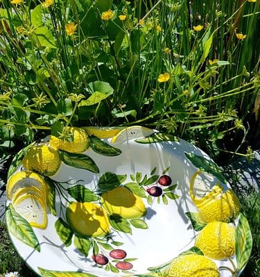 Hand-painted ceramic lemon bowl with olive branch relief in a garden of yellow wildflowers.