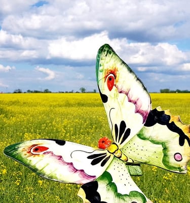 A colorful decorative butterfly metal garden stake in a blooming yellow rapeseed field under a blue sky.