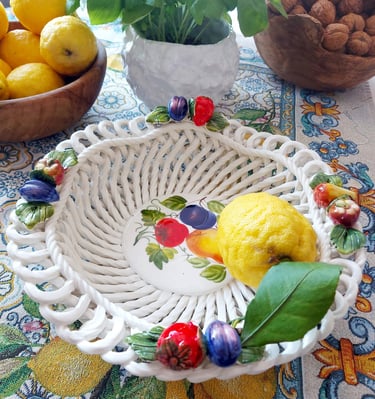 Hand-painted ceramic woven fruit bowl with a lemon on a patterned tablecloth.