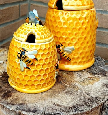 Two yellow ceramic honeycomb beehive honey pots decorated with bees on a rustic tree stump.