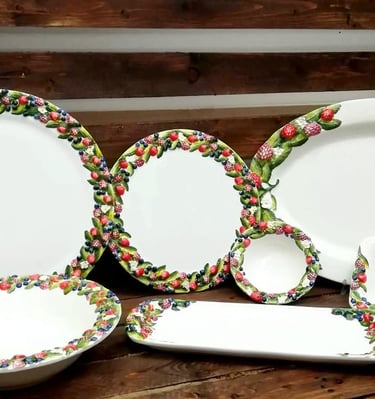 Hand-painted ceramic dinnerware set featuring 3D fruit borders with berries and leaves on a rustic wood background.