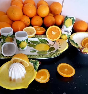 Fresh oranges and lemons arranged with ceramic citrus-themed serving dishes and a manual juicer.