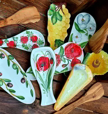 Hand-painted ceramic spoon rests with floral, fruit, and olive designs on a rustic wooden table.