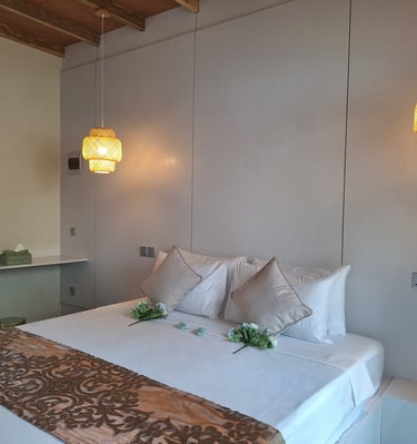Modern hotel bedroom with white linens, decorative pillows, and warm woven pendant lights.