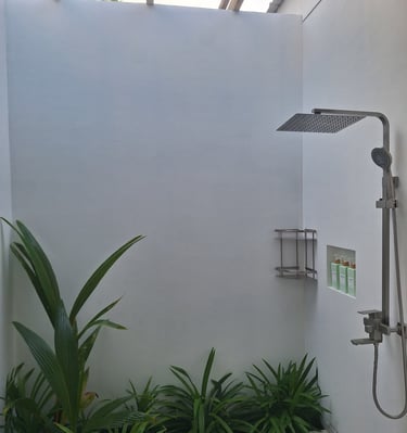 Modern outdoor rainfall shower with tropical green plants and white minimalist walls.