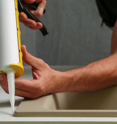 Plumber applying silicone sealant around kitchen sink installation