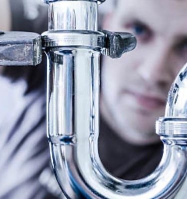 Plumber repairing pipe connection with wrench under sink