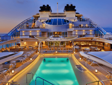 Carnival cruise ship pool deck at sunset with illuminated swimming pool and lounge areas.