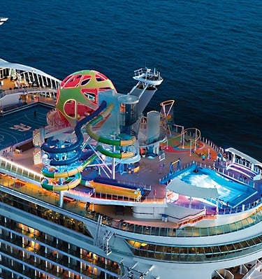 Aerial view of a Royal Caribbean cruise ship featuring water slides and a surfing simulator at sea.