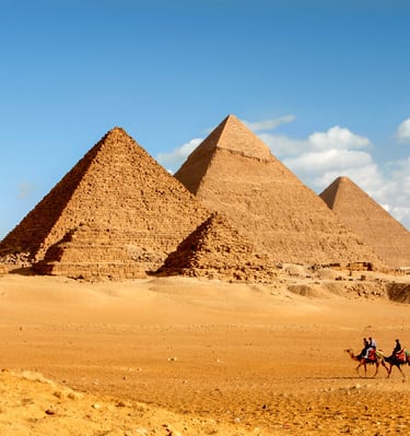 Great Pyramids of Giza in Egypt with tourists riding camels across the desert sand.
