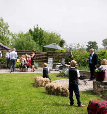 Guests enjoying an outdoor wedding reception on a sunny patio with hay bale seating.