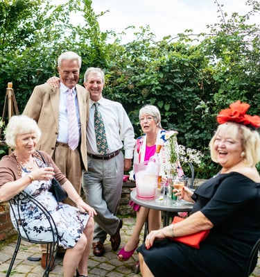 Elegant elderly guests smiling and enjoying drinks at an outdoor wedding party celebration.