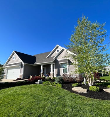 Modern single-family home with grey siding, professional landscaping, and green lawn under a clear blue sky.