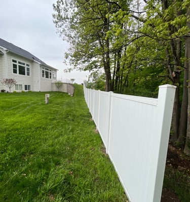 White vinyl privacy fence installed in a green backyard bordering a wooded area.