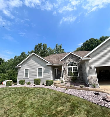 A single-family home with gray siding, stone accents, and manicured landscaping under a blue sky.