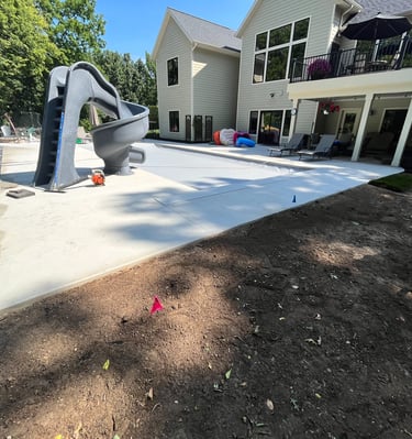 Luxury backyard pool construction featuring a gray spiral slide, concrete patio, and modern home exterior.