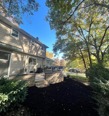 A backyard landscape featuring a stone retaining wall and fresh black mulch under autumn trees.