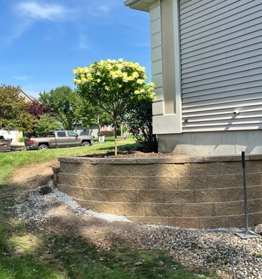 New stone retaining wall in front of a house with a flowering hydrangea tree and landscaping.