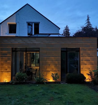 Modern copper-clad home extension with integrated outdoor lighting and large glass sliding doors.