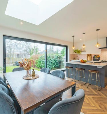 Modern open plan kitchen and dining area featuring a wood table, blue velvet chairs, and parquet flooring.