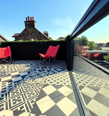 Modern rooftop terrace featuring patterned outdoor floor tiles and two red folding chairs under a clear blue sky.