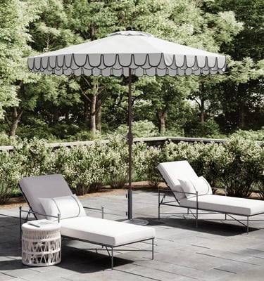 White scalloped patio umbrella with two lounge chairs on a stone terrace for outdoor luxury living.