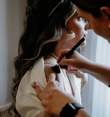 Professional makeup artist applying foundation to a bride during wedding preparations.