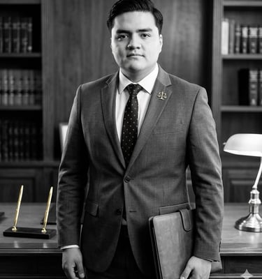 Hombre de pie con saco negro sosteniendo carpeta de cuero en una sala antigua. Imagen blanco y negro.