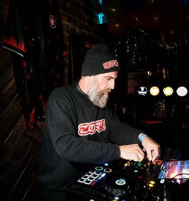 Dacarter DJ wearing headphones mixing music on a controller with a laptop at a club event.
