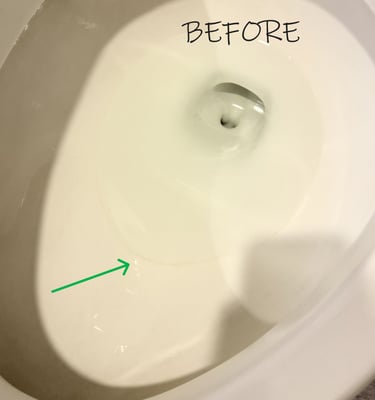Toilet bowl with a hard water ring highlighted by a green arrow before cleaning
