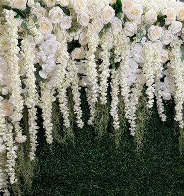Elegant white floral wall featuring roses and hanging wisteria against a lush green boxwood hedge backdrop.